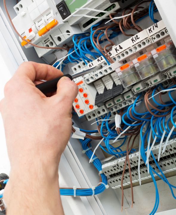 Hand bei der Arbeit an einem offenen Schaltschrank mit zahlreichen Kabeln und elektrischen Bauteilen