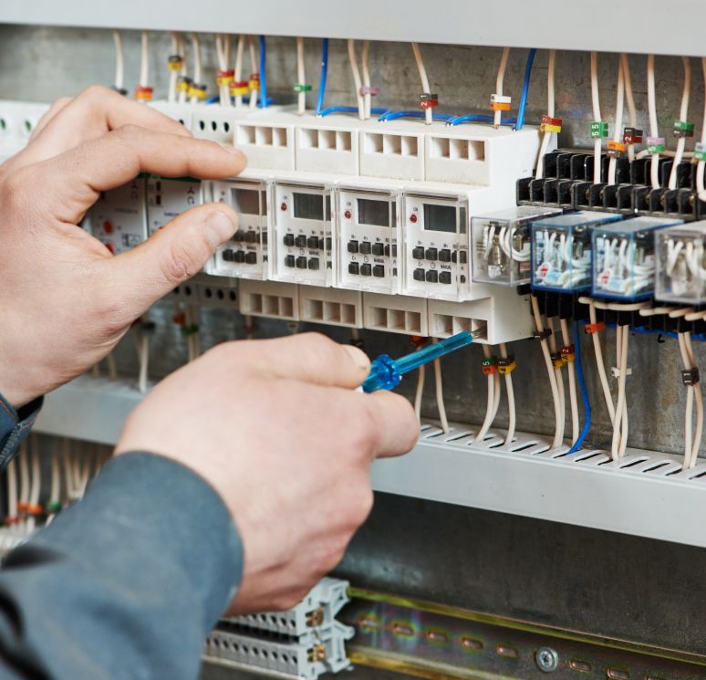 Elektriker arbeitet mit Schraubendreher an einem offenen Sicherungskasten mit zahlreichen Kabeln und Schaltmodulen