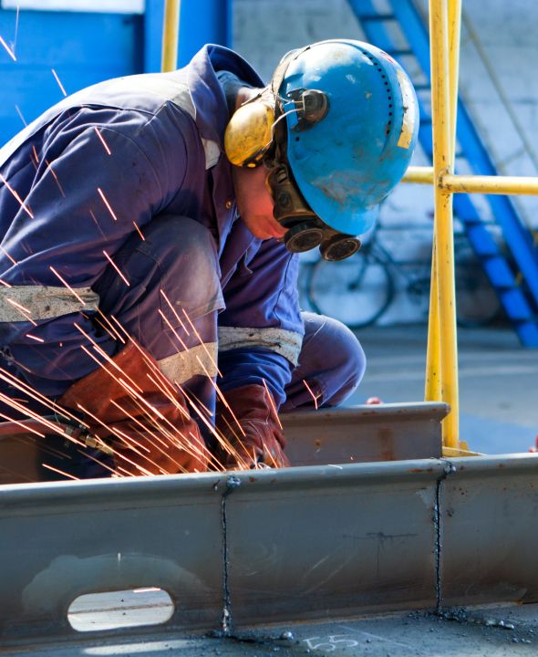 Arbeiter mit Schutzkleidung und Helm beim Schweißen einer Stahlkonstruktion